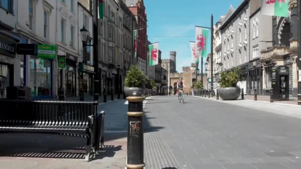 威尔士仍然被封锁 其首都加的夫是一个荒凉的城市 威尔士的国旗在微风中飘扬 所有商店都关门了 孤独的骑车人利用空旷的区域进行安全锻炼 单车车由街尾驶近 — 图库视频影像