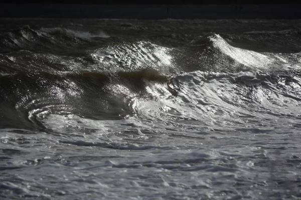 大风和涨潮的汹涌大海造成巨浪 在岩石海滩上冲撞 落日在水面上闪烁着光芒 浪花在水面上形成了薄雾 — 图库照片