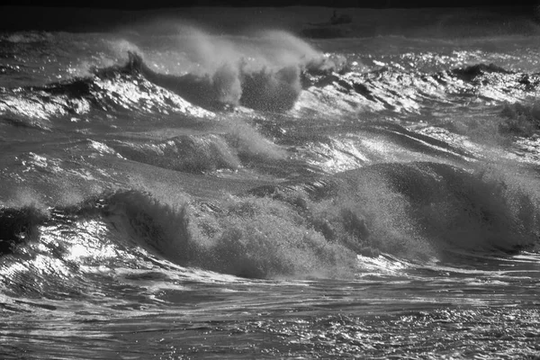 大风和涨潮的汹涌大海造成巨浪 在岩石海滩上冲撞 落日在水面上闪烁着光芒 浪花在水面上形成了薄雾 — 图库照片