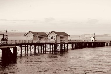 Güneş battı ve insanlar Penarth gezinti güvertesi ve iskele boyunca akşam yürüyüşünün tadını çıkarıyor. Viktorya dönemi pavyonu bu sahil kasabasında çok iyi bilinen bir simgedir ve insanlar tahta kaldırım boyunca yürümeyi severler.