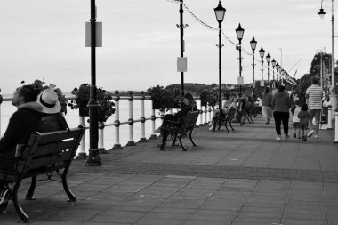 Güneş battı ve insanlar Penarth gezinti güvertesi ve iskele boyunca akşam yürüyüşünün tadını çıkarıyor. Viktorya dönemi pavyonu bu sahil kasabasında çok iyi bilinen bir simgedir ve insanlar tahta kaldırım boyunca yürümeyi severler.