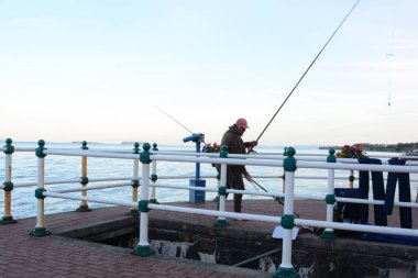 Güneş battı ve insanlar Penarth gezinti güvertesi ve iskele boyunca akşam yürüyüşünün tadını çıkarıyor. Viktorya dönemi pavyonu bu sahil kasabasında çok iyi bilinen bir simgedir ve insanlar tahta kaldırım boyunca yürümeyi severler.
