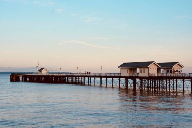 Güneş battı ve insanlar Penarth gezinti güvertesi ve iskele boyunca akşam yürüyüşünün tadını çıkarıyor. Viktorya dönemi pavyonu bu sahil kasabasında çok iyi bilinen bir simgedir ve insanlar tahta kaldırım boyunca yürümeyi severler.