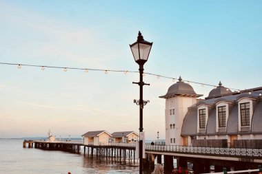 Güneş battı ve insanlar Penarth gezinti güvertesi ve iskele boyunca akşam yürüyüşünün tadını çıkarıyor. Viktorya dönemi pavyonu bu sahil kasabasında çok iyi bilinen bir simgedir ve insanlar tahta kaldırım boyunca yürümeyi severler.