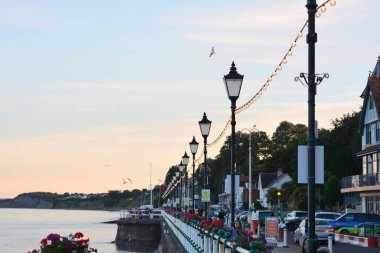 Güneş battı ve insanlar Penarth gezinti güvertesi ve iskele boyunca akşam yürüyüşünün tadını çıkarıyor. Viktorya dönemi pavyonu bu sahil kasabasında çok iyi bilinen bir simgedir ve insanlar tahta kaldırım boyunca yürümeyi severler.