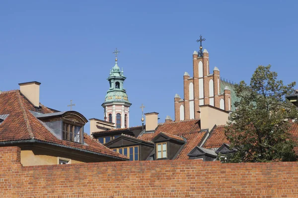 Churches, red roofs of old buildings behind red brick wall in historic Old Town, Warsaw, Poland .