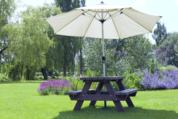 Relaxing setting in a pub garden with umbrella sitting bench next to flowers in bloom, willow trees, al fresco dining in an English countryside on a sunny summer day .