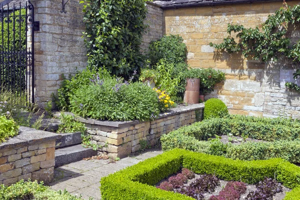 Summer vegetable and herb garden with lettuce growing in plots enclosed by trimmed hedge, herbs and fruit trees by the stone wall .