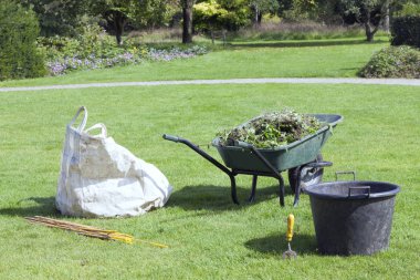 Bir yaz bahçesinde bahçe işleri, yeşil el arabası dolusu iz, beyaz çöp torbası, kova, sopalar için .