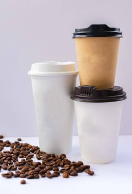 Gri arka planda kahve çekirdekleri ile kapaklı üç kağıt bardak. Model.