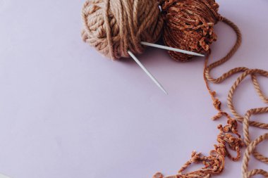 Örgü örmek için kahverengi iplik. İpliğe saplanmış örgü iğneleri. Lavanta arka planda. Hobi ve eğlence konsepti.
