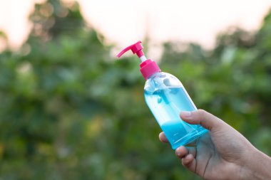 Elinde mavi alkol jeli şişesi ve doğal yeşil bir arka planı var. El yıkama için alkol jeli anti-virüs, anti-bakteriyel ve anti-virüs. Covid-19. Boşluğu kopyala.