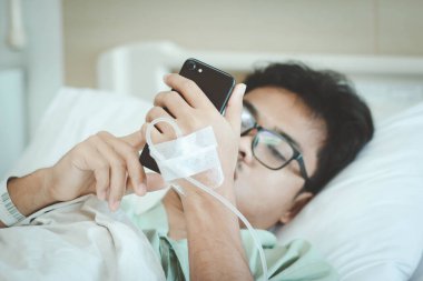 Bir erkek hasta sosyal medya için akıllı telefon kullanır ve hastanedeyken aile üyesiyle iletişime geçer. Salgın Covid-19 veya Corona virüsünden kurtulun. Seçici odak.