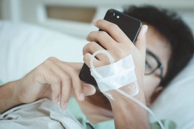 Bir erkek hasta sosyal medya için akıllı telefon kullanır ve hastanedeyken aile üyesiyle iletişime geçer. Salgın Covid-19 veya Corona virüsünden kurtulun. Seçici odak.