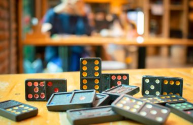 Eski siyah renkli dominoları renkli noktalarla kapatın. Düşen Siyah Domino 'lar tahta masanın üstünde, arka planda bokeh.
