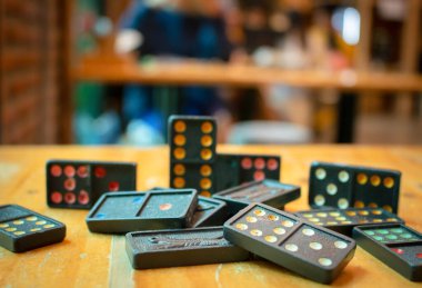 Eski siyah renkli dominoları renkli noktalarla kapatın. Düşen Siyah Domino 'lar tahta masanın üstünde, arka planda bokeh.