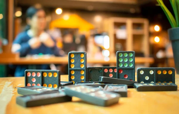 Eski siyah renkli dominoları renkli noktalarla kapatın. Düşen Siyah Domino 'lar tahta masanın üstünde, arka planda bokeh.