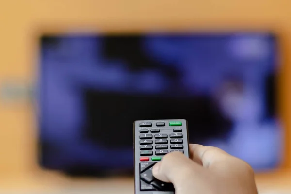 Close-up of hand with the remote control television and presses the button. Television remote control changes channels thumb on the blue TV screen.