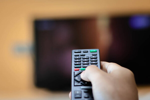 Close-up of hand with the remote control television and presses the button. Television remote control changes channels thumb on the blue TV screen.