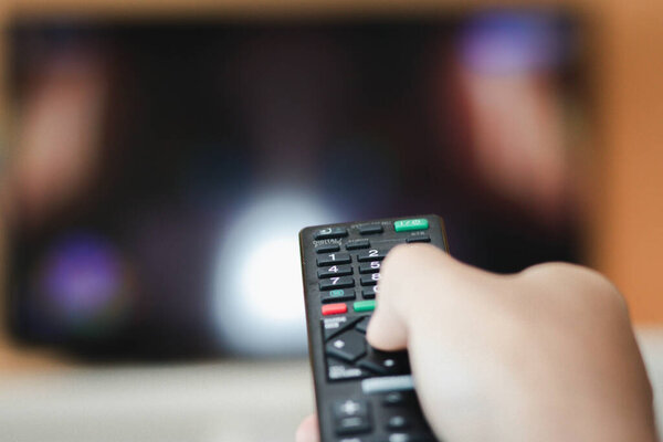 Close-up of hand with the remote control television and presses the button. Television remote control changes channels thumb on the blue TV screen.