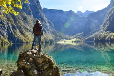 Genç yürüyüşçü taşın üzerinde duruyor ve Obersee 'ye bakıyor.