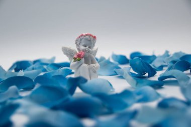 Elinde bir gül olan beyaz melek mavi suni çiçeklerle çevrili cennette gibi görünüyor.