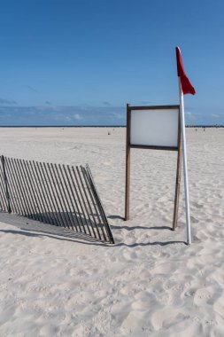 Beyaz kumsaldaki beyaz işaret levhasında fırtına eskrimi ve kırmızı bayrak
