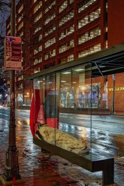 Philadelphia, PA - 10 Şubat 2020: Evsiz bir insan yağmurlu bir gecede otobüs durağındaki bankta uyuyarak bir sığınak bulur.