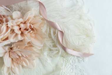 Arka planda yumuşak pembe ipek çiçeklerin, kurdeleli, dantelli ve beyaz devekuşu tüylü kopyaları var. Romantizm ya da düğün kavramı.