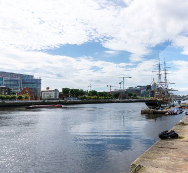 Dublin, İrlanda 'da Liffey Nehri' nde Jeanie Johnston 'ın sahnelediği kıtlık gemisi sağda turistik bir gezide kırmızı bir tur teknesi ve arka planda birkaç vinç..