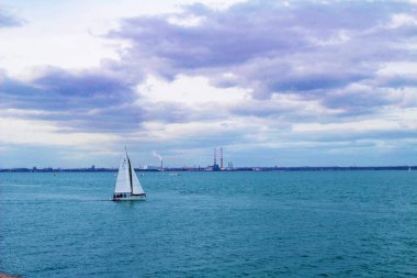 Dun Laoghaire limanından ayrılan bir yat, Dublin, İrlanda, eski Poolbeg güç istasyonunun kuleleri ve arka planda Dublin yeni yakma fırını.  