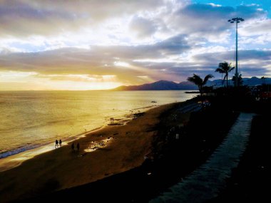 Günbatımında Puerto Del Carmen, Lanzarote, İspanya 'daki sahil, insan ve palmiye ağaçlarının silueti....