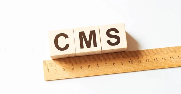 CMS letters of wooden blocks in pillar form on white background, copy space