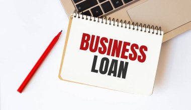 Laptop, kırmızı kalem ve beyaz arka planda BUSINESS kredisiyle birlikte not defteri