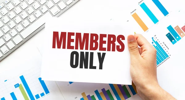 Businessman holding a card with text MEMBERS ONLY. Keyboard, diagram and white background