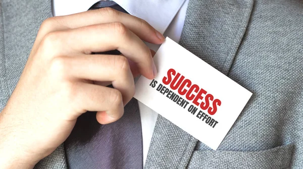 Businessman putting a card with text Success is dependent on effort in the pocket