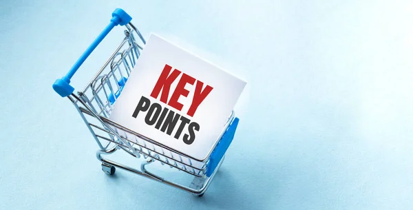 Shopping cart and text key points on white paper note list. Shopping list concept on blue background.