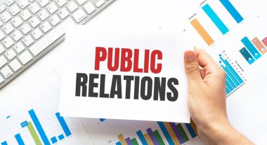 Klavye, diyagram ve beyaz arkaplan içeren PUBLIC ilişkili bir kart tutan işadamı