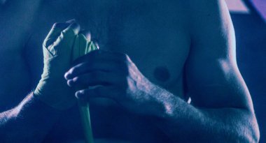 Kaslı dövüşçü eline bant bağlayıp boks yapmaya hazırlanıyor.