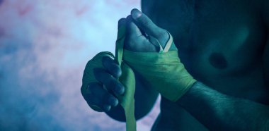 Kaslı dövüşçü eline bant bağlayıp boks yapmaya hazırlanıyor.