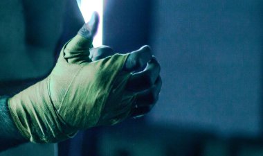 Kaslı dövüşçü eline bant bağlayıp boks yapmaya hazırlanıyor.