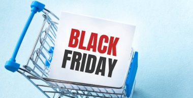 Alışveriş arabası ve Kara Cuma 'yı kâğıt üzerinde beyaz not listesine yaz. Mavi arkaplanda alışveriş listesi kavramı.