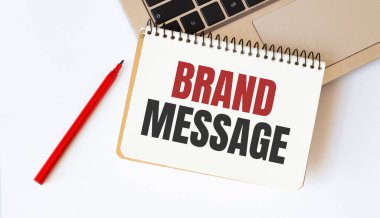 Laptop, kırmızı kalem ve beyaz arkaplanda BRAND MESAGE yazılı not defteri