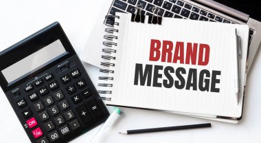 Dizüstü bilgisayar, hesap makinesi, kalem ve not defteri beyaz arkaplanda BRAND MESSAGE metni