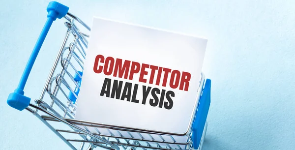 Alışveriş arabası ve COMPETITOR ANALYSIS 'i beyaz kağıt üzerinde not listesine yaz. Mavi arkaplanda alışveriş listesi kavramı.