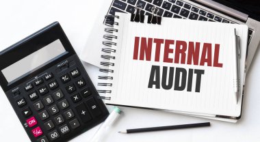 Beyaz arkaplanda INTERANL AUDIT yazılı dizüstü bilgisayar, hesap makinesi, kalem ve not defteri
