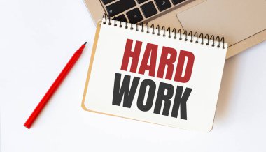 Laptop, kırmızı kalem ve beyaz arkaplanda HARD Work metniyle birlikte not defteri