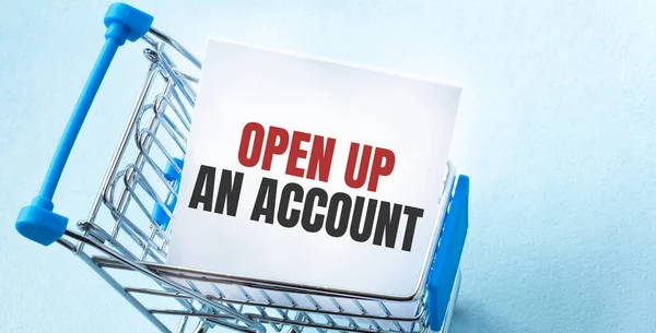 Shopping cart and text OPEN UP AN ACCOUNT on white paper note list. Shopping list concept on blue background.