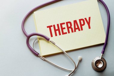 Mor arkaplanda, üzerinde THERAPY metni olan sarı listeli bir steteskop var.