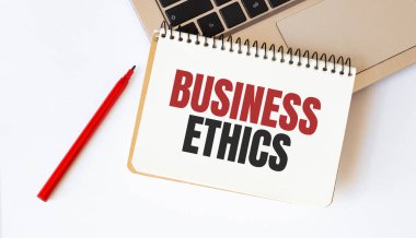 Diz üstü bilgisayar, kırmızı kalem ve beyaz arkaplandaki BUSINESS ETHICS yazılı not defteri